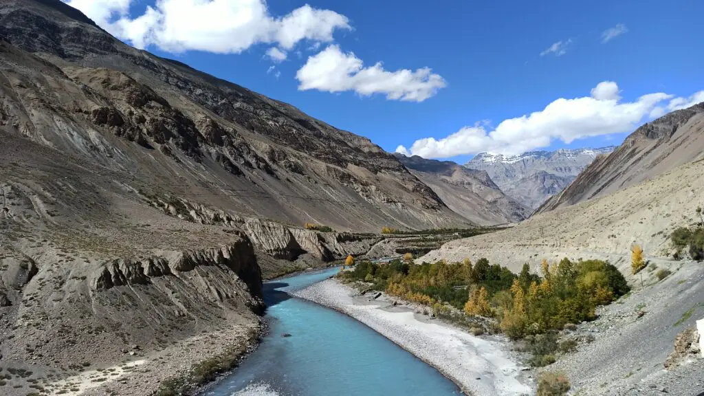 view of spiti river flowing through the mountains clear blue water and blue sky with some clouds
