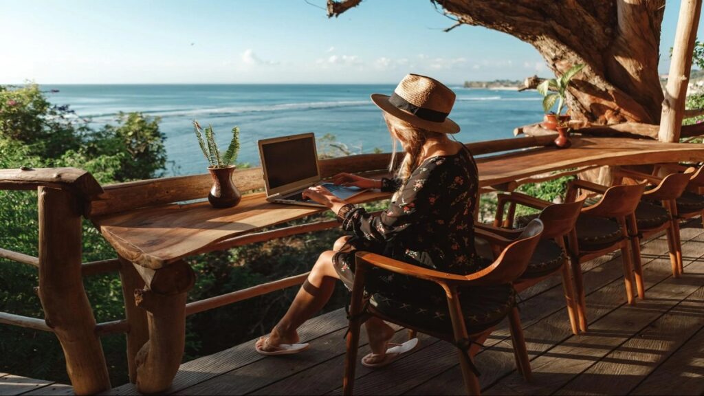 digital nomad woman working at laptop on beach, Guide to Digital Nomadism and "Workations"