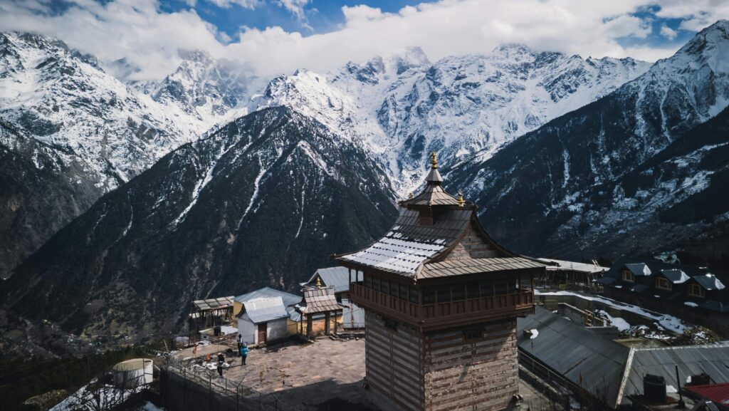 Stunning view of Kinnaur Kailash temple and snow-covered Himalayan mountains under a vibrant sky.