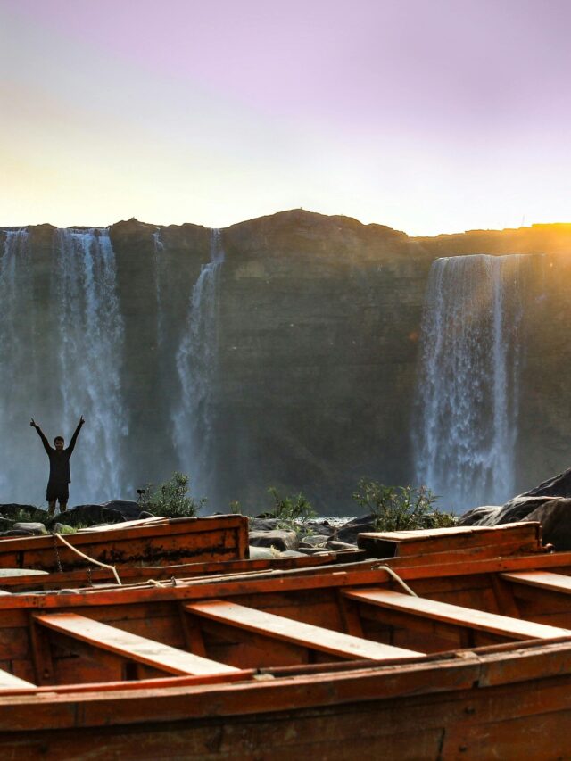 A stunning sunset over a cascading waterfall with a boat in the foreground and a celebrating figure.