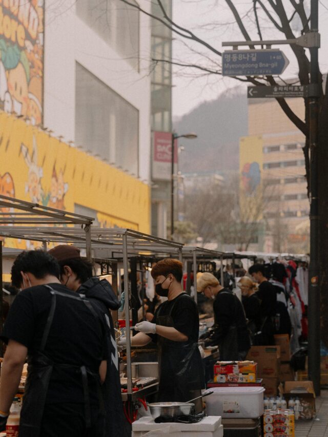 Urban street food market with vendors selling diverse cuisine in city setting.